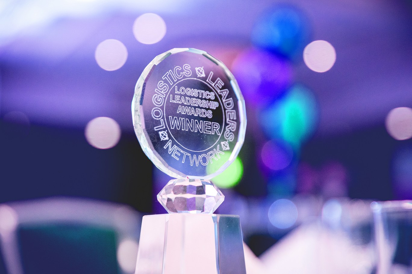 Crystal Logistics Leadership Awards winner trophy against a softly blurred backdrop of colourful event lights.