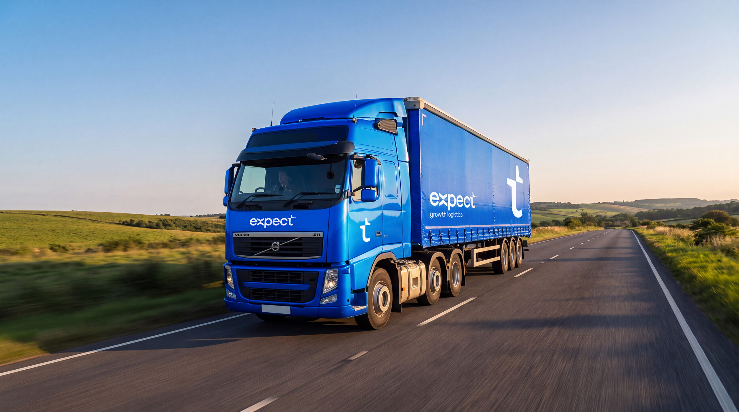 Blue Expect Logistics lorry travelling along a rural road through rolling countryside.
